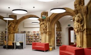rote Sofas im Lesebereich der Heinrich-Schulz-Bibliothek, Sandsteinsäulen und Bücherregale in einem halbrunden Raum
